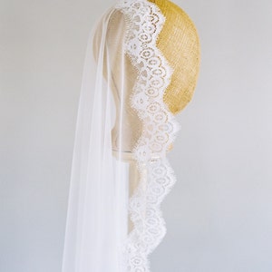 May include: A white bridal veil with a delicate lace trim. The veil is draped over a mannequin head.