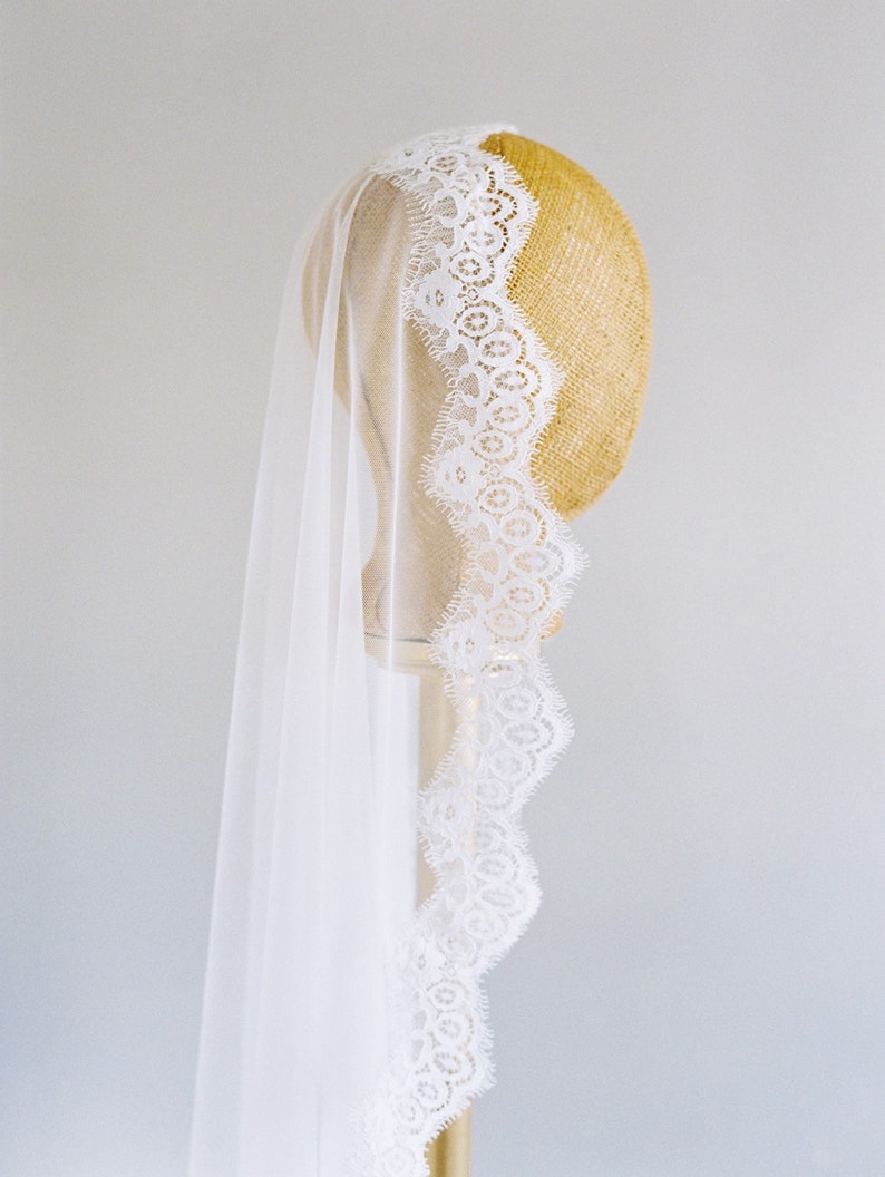 May include: A white bridal veil with a delicate lace trim. The veil is draped over a mannequin head.