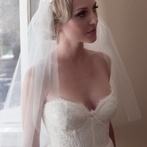 May include: A bride wearing a white strapless wedding dress with a lace bodice and a white veil with a floral design.