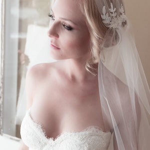May include: A bride wearing a white strapless wedding dress with lace detailing and a white veil with a floral design.