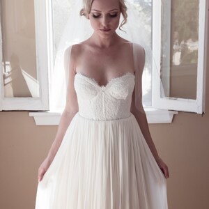 May include: A bride wearing a white strapless wedding dress with a lace bodice and a flowing skirt. She is wearing a veil and has her hair pulled back.