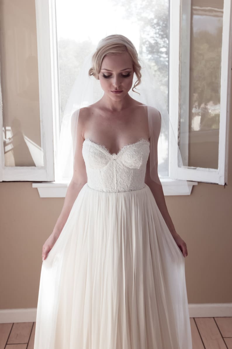May include: A bride wearing a white strapless wedding dress with a lace bodice and a flowing skirt. She is wearing a veil and has her hair pulled back.