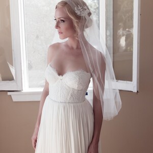 May include: A bride wearing a white strapless wedding dress with a lace bodice and a flowing skirt. She is wearing a white veil with a floral design and has her hair pulled back.