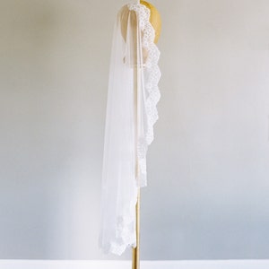 May include: A white bridal veil with a delicate lace trim, displayed on a gold stand.
