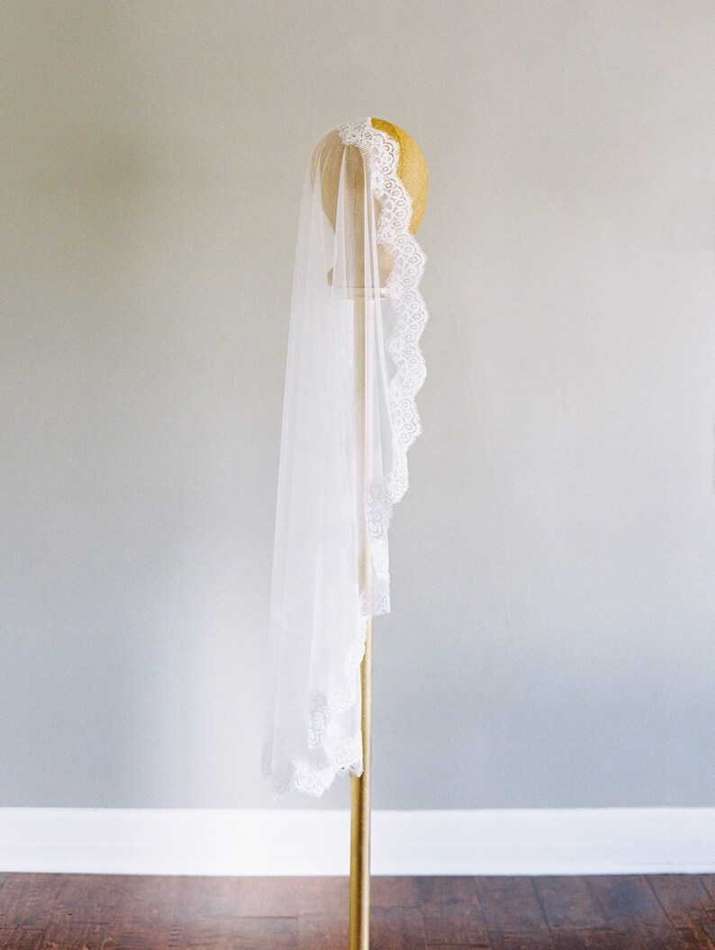 May include: A white bridal veil with a delicate lace trim, displayed on a gold stand.