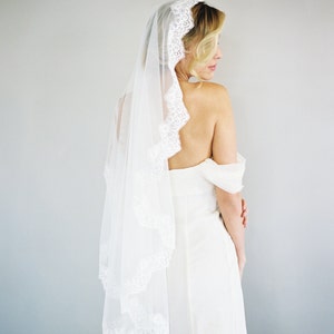 May include: A white bridal veil with a delicate lace trim. The veil is draped over the back of the bride's head and falls down her back.