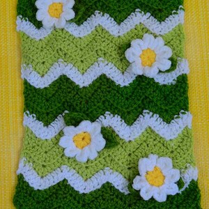 May include: A handmade crochet blanket featuring a green and white chevron pattern with white daisy accents. The blanket has a scalloped edge and is made with various shades of green yarn. The daisies have yellow centers.