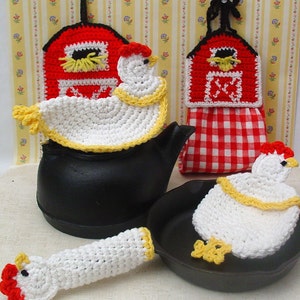 May include: Set of three crocheted chicken pot holders. The pot holders are white with yellow accents and feature a red and white barn design. The pot holders are displayed on a black cast iron teapot and skillet.