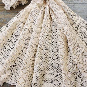 May include: A cream-colored crocheted tablecloth with a delicate floral pattern. The tablecloth is made of a lightweight, airy fabric and has a scalloped edge.