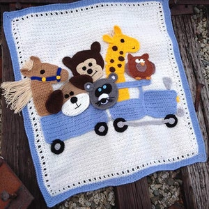 May include: A crocheted baby blanket with a blue border and a white center. The blanket features a blue toy train with a giraffe, bear, horse, cat, and owl riding on top.