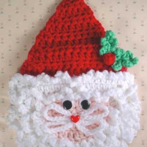 May include: Crocheted Santa Claus ornament with a red hat, white beard, and pink face. The ornament has black eyes and a red heart-shaped nose.