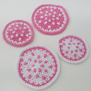 May include: Four crocheted pink and white coasters with a polka dot pattern. The coasters are round and have a white border.
