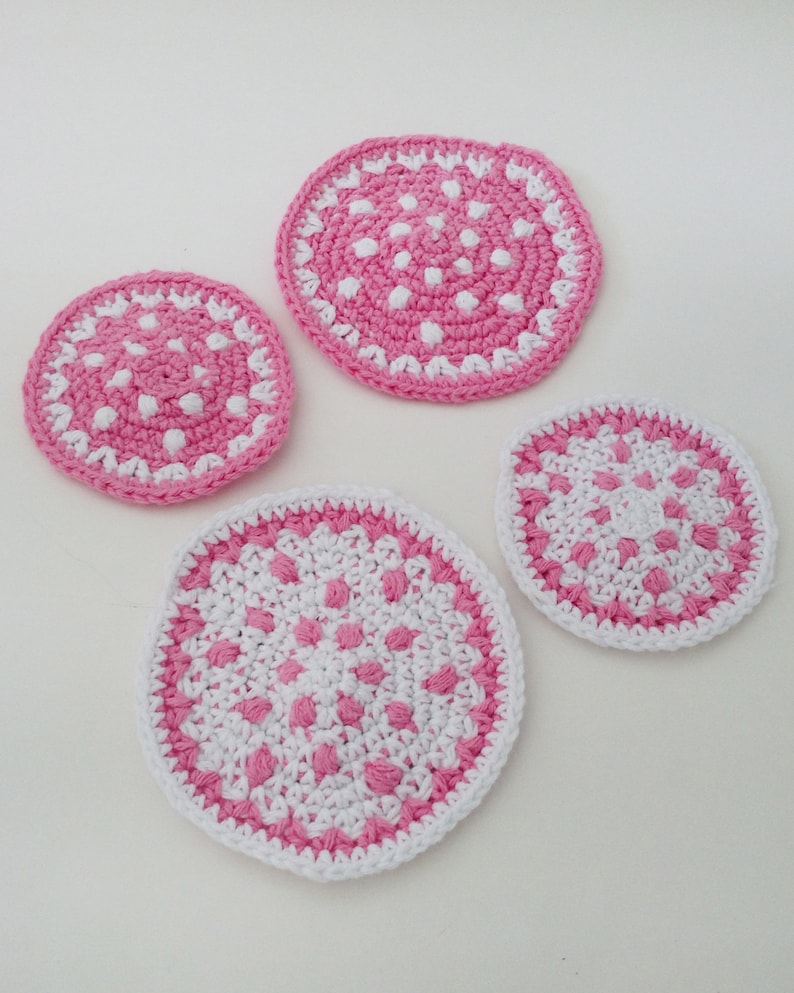 May include: Four crocheted pink and white coasters with a polka dot pattern. The coasters are round and have a white border.