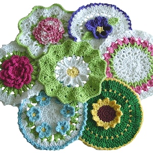 Op de afbeelding: Een verzameling gehaakte doilies met verschillende bloemenmotifs, waaronder een madeliefje, een zonnebloem, een roos en een viooltje. De doilies zijn gemaakt in tinten wit, groen, roze, geel en blauw.
