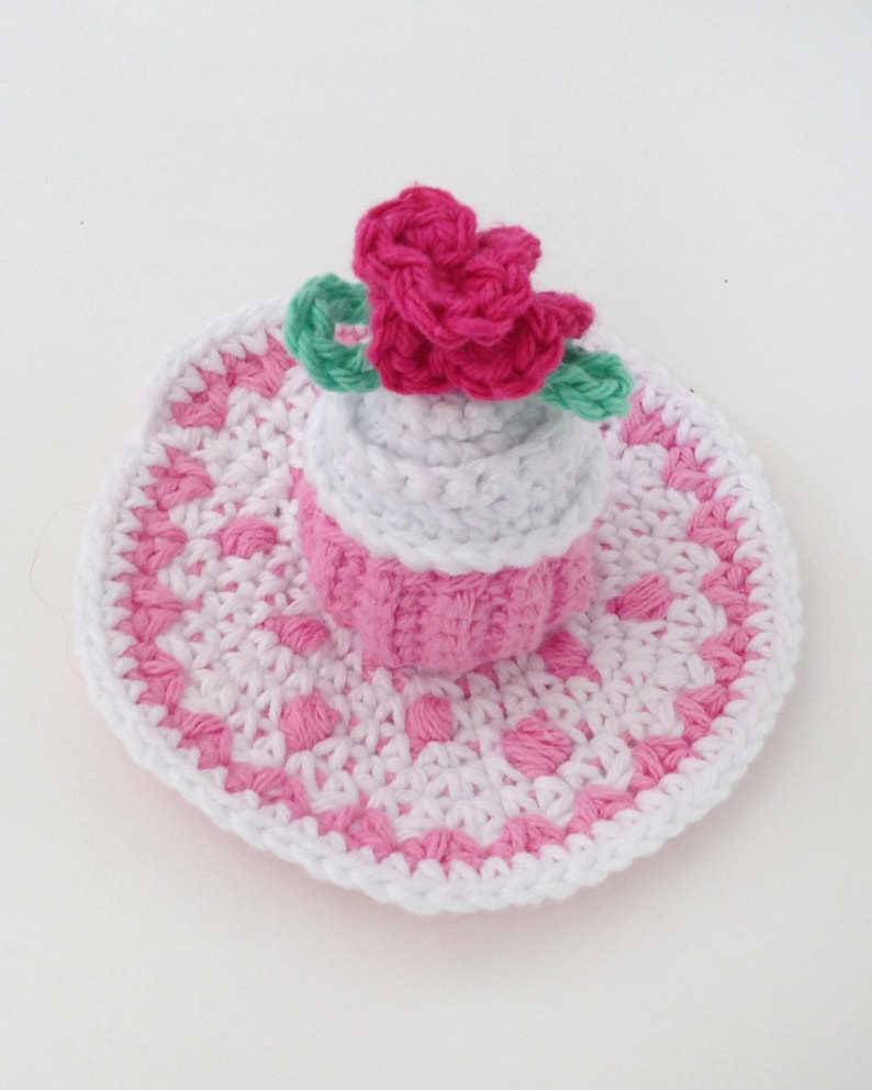 May include: A pink and white crocheted hat with a pink flower on top. The hat is made with a delicate stitch pattern and has a wide brim.