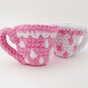 May include: Two crocheted teacups, one pink with white polka dots and one white with pink polka dots.