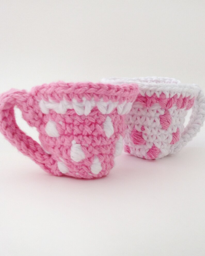 May include: Two crocheted teacups, one pink with white polka dots and one white with pink polka dots.