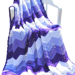 May include: A crocheted blanket with a chevron pattern in shades of purple, blue, and white. The blanket is draped over a white chair.