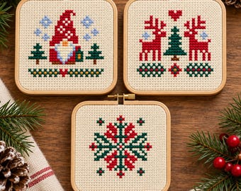 May include: Three square wooden embroidery hoops containing cross-stitch patterns on cream fabric. One features a gnome with a red hat, one shows two red reindeer flanking a green tree, and the third displays a red and green snowflake design.