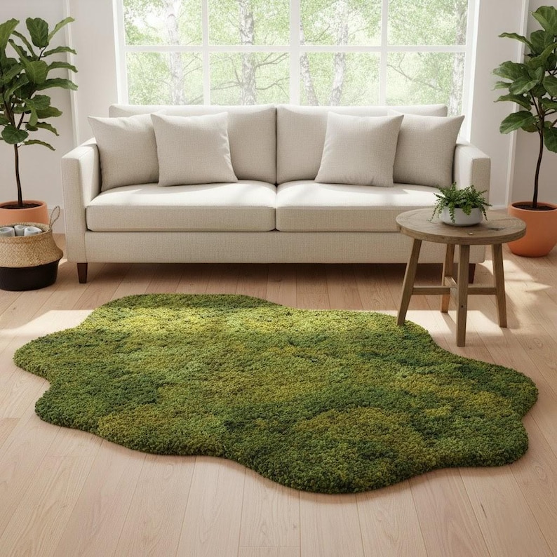 May include: A green, irregularly shaped rug resembling moss, placed on a light wood floor. A beige sofa with pillows is in the background, along with a small wooden side table and potted plants. The rug adds a natural element to the room.