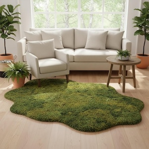 May include: A green, irregularly shaped rug resembling a patch of moss sits on a light wood floor. The rug is in front of a cream-colored sofa and armchair. Potted plants and a small wooden side table complete the living room scene.