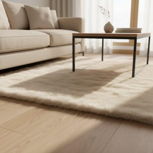 May include: A beige living room scene featuring a plush, cream-colored rug, a light-colored sofa with pillows, and a square coffee table with a dark frame. The room has hardwood floors and natural light.