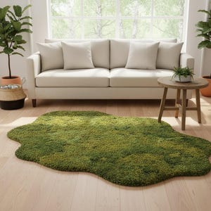 May include: A green, irregularly shaped rug with a moss-like texture sits on a light wood floor. A beige sofa with four pillows is in the background, along with a small wooden side table and potted plants.