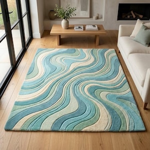 May include: A rectangular area rug featuring a textured, wavy pattern in shades of light blue, teal, sage green, and cream. The design consists of flowing, carved-look lines that create a sense of movement across the entire surface of the rug.