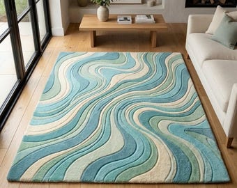 Puede incluir: Una alfombra rectangular con un patrón ondulado y texturizado en tonos azul claro, verde azulado, verde salvia y crema. El diseño consiste en líneas fluidas con aspecto tallado que crean una sensación de movimiento por toda la superficie.