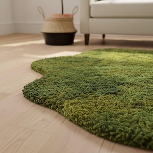 May include: A green, irregularly shaped rug with a textured, moss-like appearance. The rug's color transitions from a lighter green to a darker shade, creating depth. The rug is placed on a light-colored wooden floor.