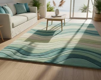 Puede incluir: Una alfombra rectangular con un diseño ondulado en tonos de azul, verde y crema. La alfombra está colocada sobre un suelo de madera clara en un salón. También se ven un sofá blanco y una pequeña mesa de madera.