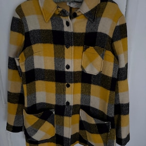 May include: A yellow, black, and cream checked jacket with a collared neckline, two front pockets, and black buttons. The jacket is hanging on a metal hanger against a white background. The jacket is a vintage style.