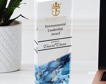May include: A clear acrylic award with a blue and gold abstract design. The award reads "Elite Title Solutions LLC Environmental Leadership Award Awarded to David Dean".
