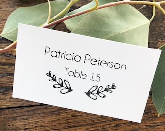 May include: White place card with black text that reads "Patricia Peterson Table 15" with a simple black floral design.