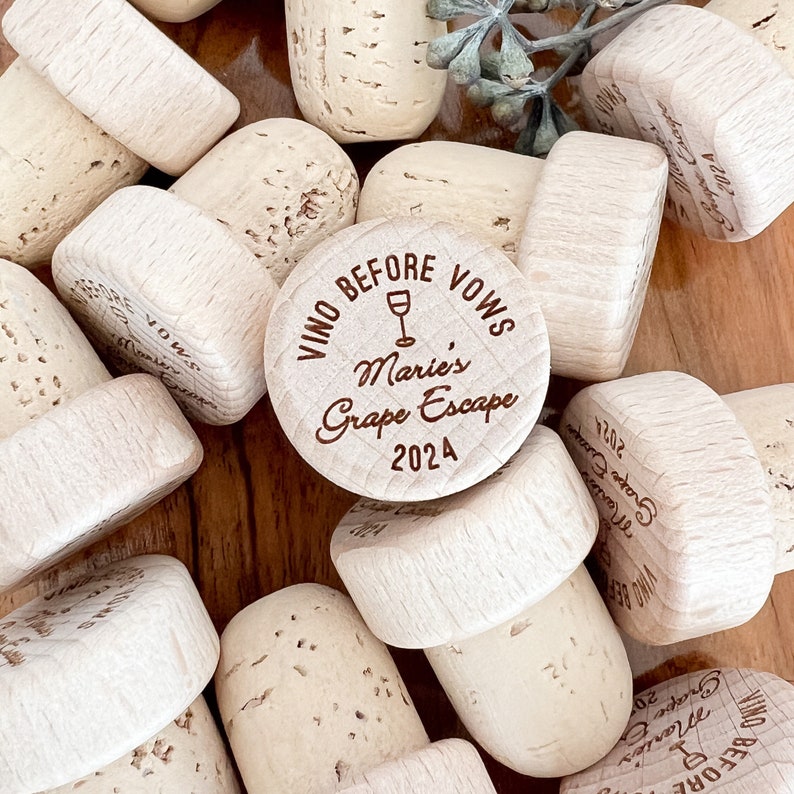 May include: A selection of natural cork bottle stoppers, some engraved with the text "Vino Before Vows" and "Marie's Grape Escape 2024". The stoppers are light brown and beige, featuring a wine glass graphic.