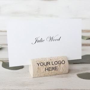 May include: Cork place card holder with the text "YOUR LOGO HERE" on the front. A white card with the name "Julie Wood" is displayed on the holder.