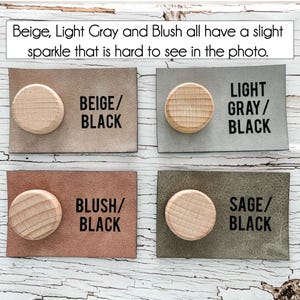 May include: Four rectangular leather samples with wooden knobs. The samples are beige, light grey, blush, and sage. Each sample has a corresponding text label in black: BEIGE/BLACK, LIGHT GRAY/BLACK, BLUSH/BLACK, and SAGE/BLACK. The text at the top says "Beige, Light Grey and Blush all have a slight sparkle that is hard to see in the photo."
