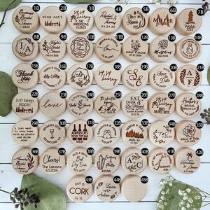 Some design options to choose from. Forty-two round wooden wine bottle stoppers with various engraved designs and text. Some of the designs include wine glasses, flowers, and floral branches. Some of the text include names and dates, initials, Sip Sip Hooray, Cheers, Eat Drink and Be Married, Put a cork in it, and more.