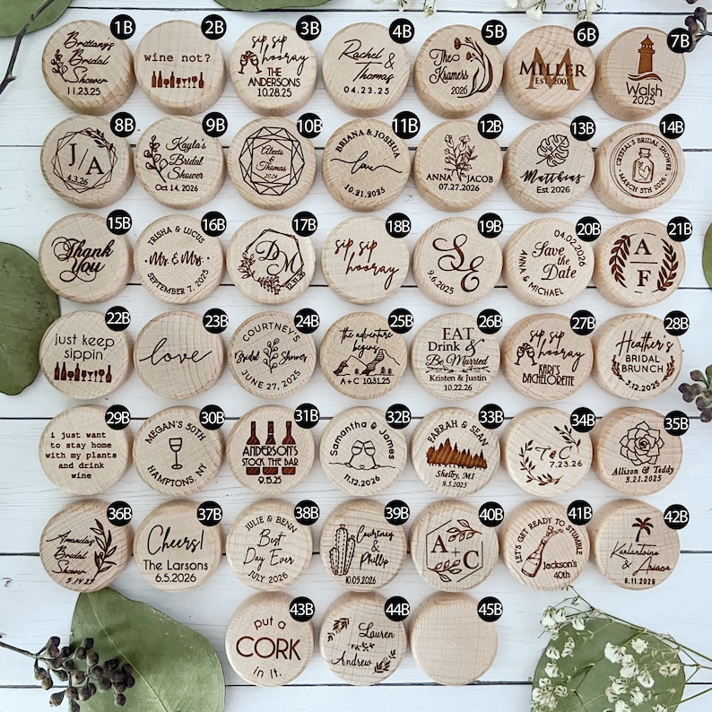 Some design options to choose from. Forty-two round wooden wine bottle stoppers with various engraved designs and text. Some of the designs include wine glasses, flowers, and floral branches. Some of the text include names and dates, initials, Sip Sip Hooray, Cheers, Eat Drink and Be Married, Put a cork in it, and more.