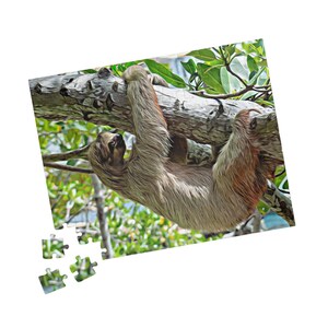 May include: A sloth hanging from a tree branch, depicted in a puzzle. The sloth has light brown fur and is hanging upside down. The puzzle pieces are in the lower left corner, with a background of green leaves and blue sky.