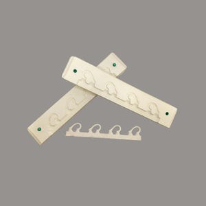 May include: Three off-white plastic coat racks with a series of curved hooks. Two racks are crossed, and one is separate. Each rack has green circular accents at the ends. The hooks are designed to hold clothing items.