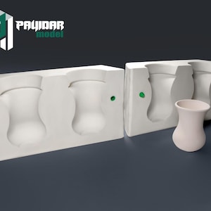 May include: Three white ceramic molds for making vases, with one finished vase sitting on a gray surface. The molds are rectangular and have a smooth, white finish. The finished vase is a simple, elegant design.