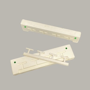 Puede incluir: Dos perchas de plástico blanquecino con pequeños ganchos. Una está encima de la otra, con una tercera encima. Cada una tiene un punto verde. Diseñado para ropa.