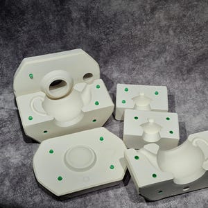 Może przedstawiać: Pięć białych form ceramicznych do tworzenia zestawów czajnika i filiżanki. Formy mają małe zielone kropki wokół krawędzi.