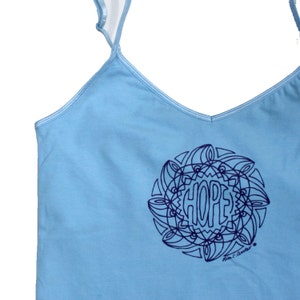 May include: A light blue tank top with a navy blue mandala design featuring the word "HOPE" in the center. The design is signed "Rian C. Andes."