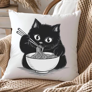 Op de afbeelding: Een wit kussen met een zwart-witte illustratie van een kat die noedels eet uit een kom met eetstokjes.