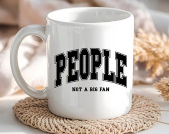 May include: White ceramic mug with black text that reads "PEOPLE NOT A BIG FAN".
