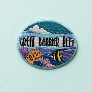 Può includere: Toppa ricamata circolare con la scritta "Great Barrier Reef". Il disegno raffigura una scena sottomarina con un pesce, coralli e un oceano e cielo blu.