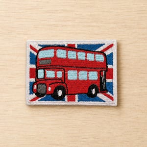 May include: Embroidered patch featuring a red double-decker bus with blue windows, set against a Union Jack flag background. The patch is rectangular with a white border, showcasing a classic British symbol.