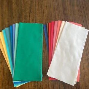 May include: A collection of fabric swatches in various colors, including yellow, blue, green, red, and white. The swatches are arranged in a fan shape, with the white swatch at the bottom.